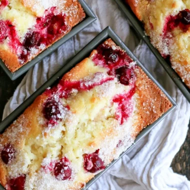 Loaf of cozy cranberry quick bread with fresh cranberries on a wooden table.