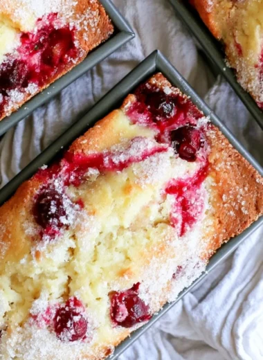 Loaf of cozy cranberry quick bread with fresh cranberries on a wooden table.