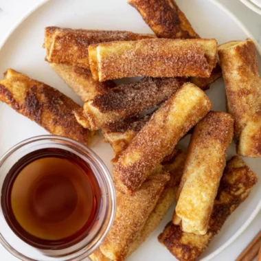 Delicious French Toast Roll-Ups served with syrup and powdered sugar.