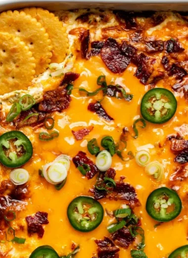 Creamy jalapeno popper dip in a bowl, garnished with jalapenos and served with chips.