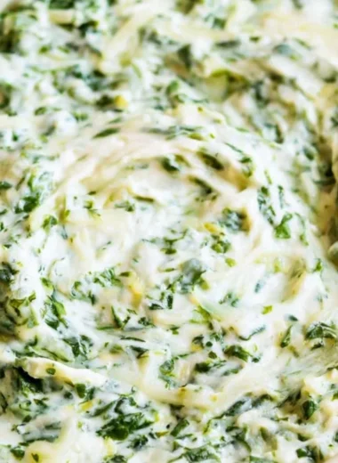 Creamy spinach dip served in a bowl with fresh vegetables and chips on the side.