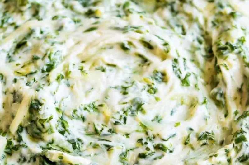 Creamy spinach dip served in a bowl with fresh vegetables and chips on the side.