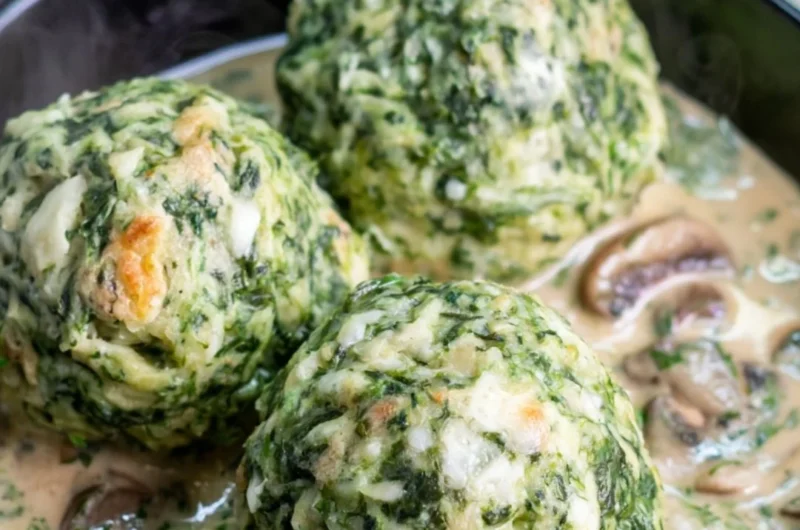 Plate of spinach dumplings covered in mushroom sauce, garnished with herbs.